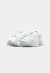 Hvite athletic sneakers med mesh- og skinnoverflater, snøring og teksturerte såler. Har diskret merkevare og rund tå.
