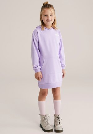 Levandų spalvos su gobtuvu džemperio suknelė su kengūros kišene, ilgomis rankovėmis ir ribomis rankogaliuose, derinama su pilkais auliukiniais batais ir šviesiai rožiniais kelių aukščio kojinaitėmis.