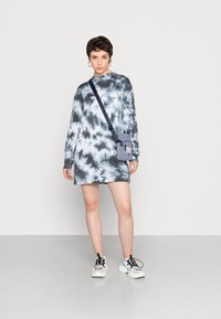 Vestido de manga comprida em tie-dye preto e branco, com um corte descontraído. Acompanhado por uma pequena mala cinza a tiracolo e ténis chunky brancos.