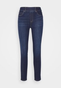 Tamno plave, uske traperice s visokim strukom. Ima četiri džepa i kontrastne zlatne šavove duž šavova. Glatka denim tekstura.
