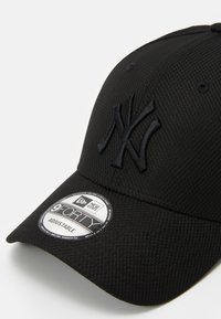 Casquette de baseball noire en tissu texturé, avec un logo "NY" noir en relief et une étiquette circulaire indiquant qu'il s'agit d'un modèle ajustable 9FORTY.