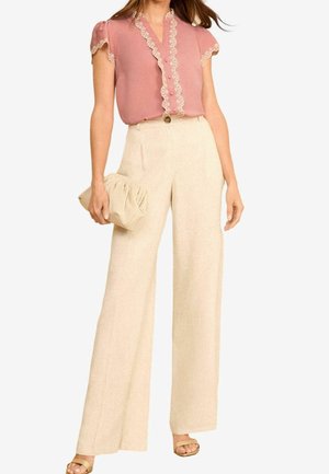 Femme portant un chemisier rose à bordure en dentelle rentré dans un pantalon large crème taille haute, tenant une pochette beige.
