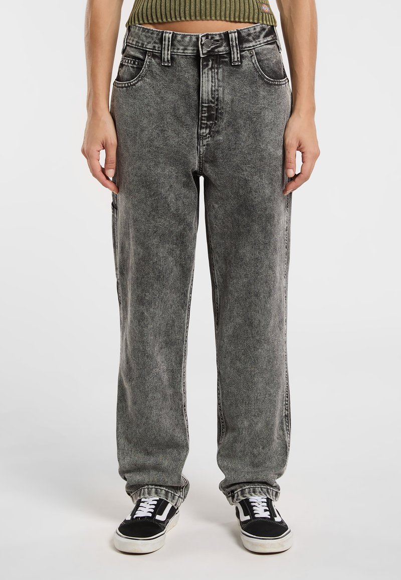 Pantalones de mezclilla gris tratado con ácido, de corte holgado, cintura alta y cinco bolsillos. Costuras negras y puños enrollados. Combinados con zapatillas negras.