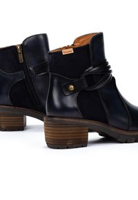 Botas de cuero negro hasta el tobillo con cremallera lateral, con punta redonda, tacón de madera apilada y una correa decorativa con un botón de acento.