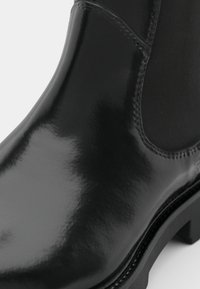 Fekete lakkbőr bokacsizma sima, fényes felülettel, elasztikus oldalpanelekkel és vastag fekete gumitalppal.