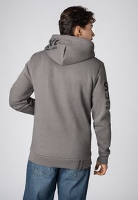 Grijze hoodie met een grote capuchon, ribbelboorden en zoom, en zwarte tekstaccenten op de mouwen. Glad textuur met een ontspannen pasvorm.