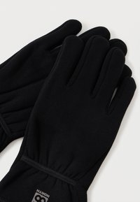 Um par de luvas de inverno em fleece preto com pulso elástico sobre um fundo neutro.
