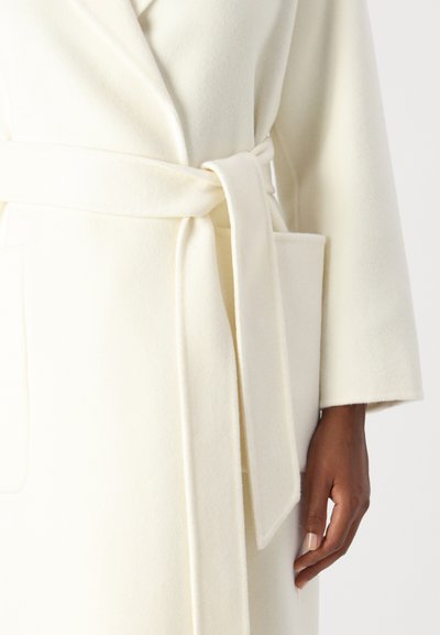 Weißer Wollmantel mit Wickeldesign, weiten Ärmeln, einem Gürtel in der Taille und einer Tasche auf der Vorderseite. Weicher, strukturierter Stoff.