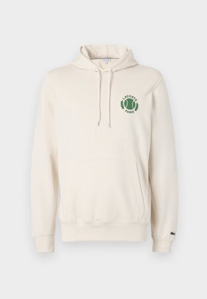 Bijela dukserica s kapuljačom s prednjim kengur džepom, zeleni izvezeni logo s motivom tenisa i natpisom "LACOSTE PARIS", te rebrasti manžeti.