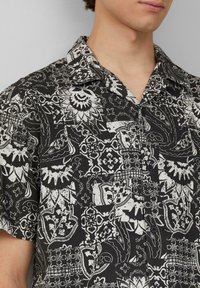 Zwart-wit korte mouwen shirt met ingewikkelde bloem- en paisleypatronen, met een relaxte kraag en knoopsluiting.
