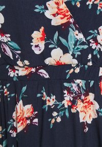 Tissu à motif floral en bleu marine foncé, présentant de grandes fleurs jaunes, rouges et blanches, avec des feuillages, et un détail de texture froncée.