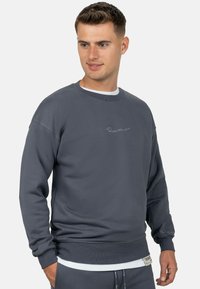 Donkergrijze sweatshirt met een ronde hals, ribgebreide mouwen en onderkant. Voorzien van een subtiele geborduurde logo op de borst. Zachte stoftextuur.