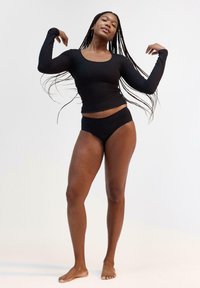 Maglietta nera a maniche lunghe con scollatura a giro e texture a costine abbinata a slip bikini neri a vita alta. Design semplice e minimalista.