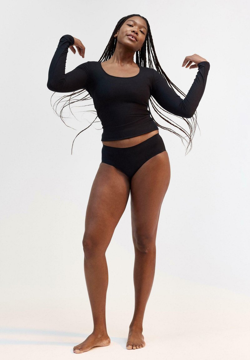 Maglietta nera a maniche lunghe con scollatura a giro e texture a costine abbinata a slip bikini neri a vita alta. Design semplice e minimalista.