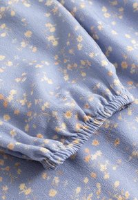 Tissu bleu clair avec petits motifs floraux jaunes et blancs, présentant un détail de poignet élastique froncé.