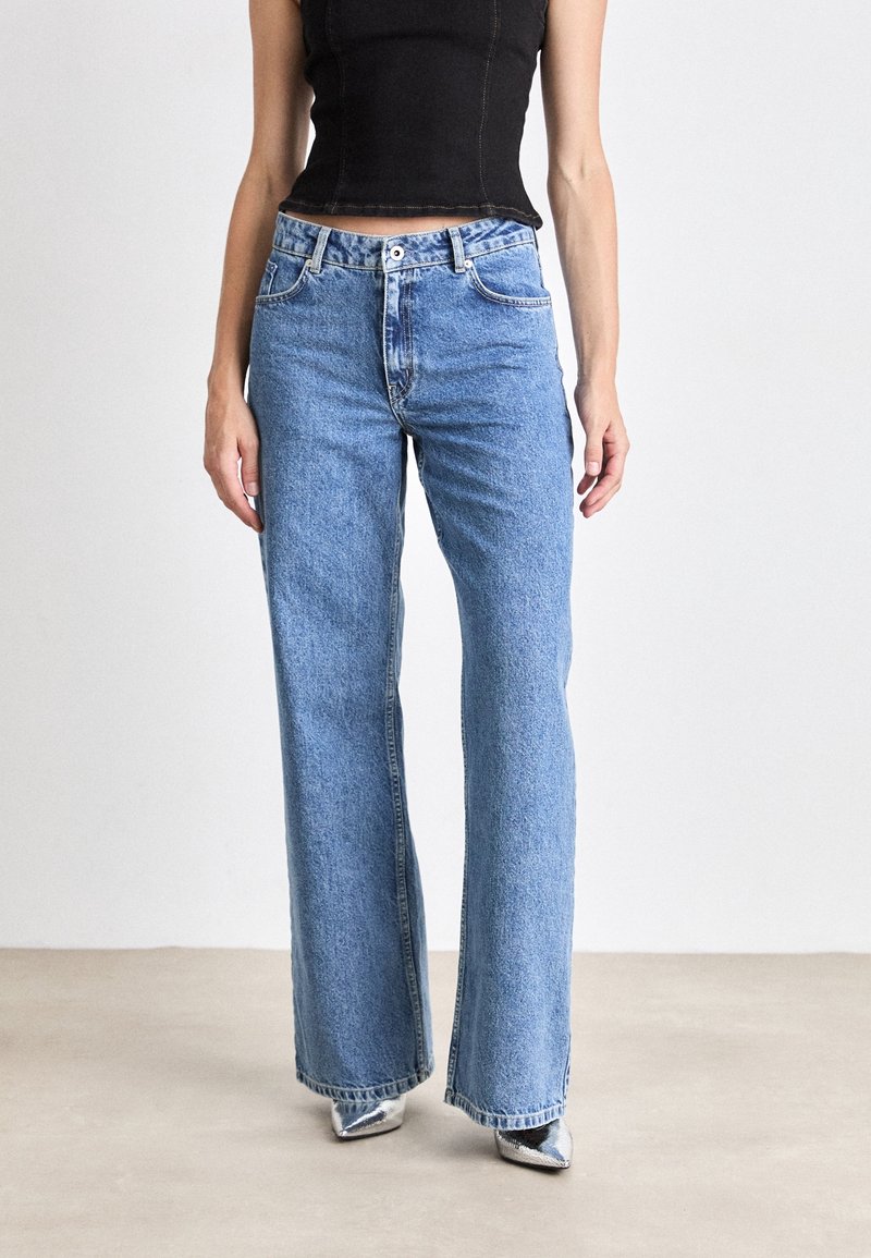 Bredbenta blå jeans i denim, med hög midja, fem fickor och tvättat utseende, som bärs tillsammans med silverfärgade klackskor.