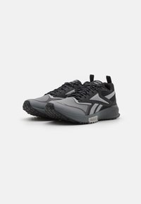 Scarpe sportive con una tomaia in rete nera e grigia, suola resistente, accenti testurizzati e dettagli riflettenti, progettate per prestazioni e comfort.