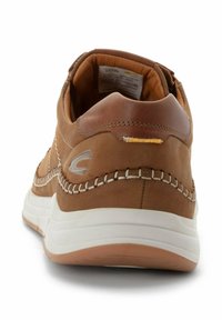 Braune Ledersneaker mit weißer Sohle, genähten Details und einem kleinen gelben Akzent in der Nähe der Ferse. Rundliche Form mit gepolstertem Innenraum.