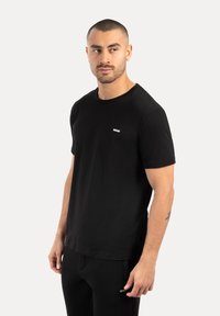 Czarny bawełniany T-shirt z okrągłym dekoltem, krótkimi rękawami i małym białym logo na piersi. Gładka faktura, prosty design, klasyczny krój.