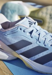 Hellblaue Adidas Adizero Counterblast Sportschuhe mit weißen Schnürsenkeln und dunklem Drei-Streifen-Logo auf einer Holzoberfläche.