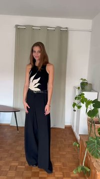 Svarta vida byxor i kombination med en ärmlös svart topp som har en vit växtdesign. Slät tyg, minimala detaljer, figurnära siluett.