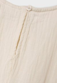 Tissu de couleur crème avec une finition texturée, présentant une patte de boutonnage verticale et un seul bouton rond au niveau du col.