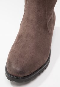 Botte en daim marron avec un bout arrondi et une semelle épaisse en caoutchouc noir sur fond blanc.
