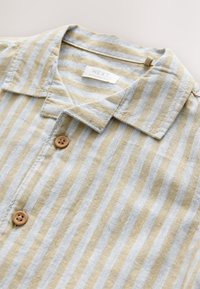 Camisa de manga corta a rayas en tejido suave, con franjas alternas amarillas y grises, cuello y cierre con un botón marrón.