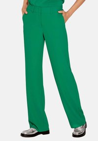 Groene wijde broek met een vlakke voorkant, zijzakken en een gladde textuur. Gecombineerd met glanzende zilveren schoenen, weergegeven tegen een effen achtergrond.