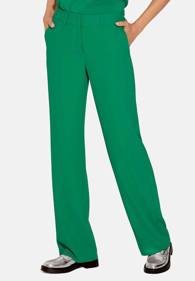 Groene wijde broek met een vlakke voorkant, zijzakken en een gladde textuur. Gecombineerd met glanzende zilveren schoenen, weergegeven tegen een effen achtergrond.