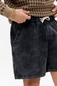 Shorts en velours côtelé gris foncé avec une texture côtelée, dotés de deux poches latérales et d'une taille avec cordon de serrage blanc.