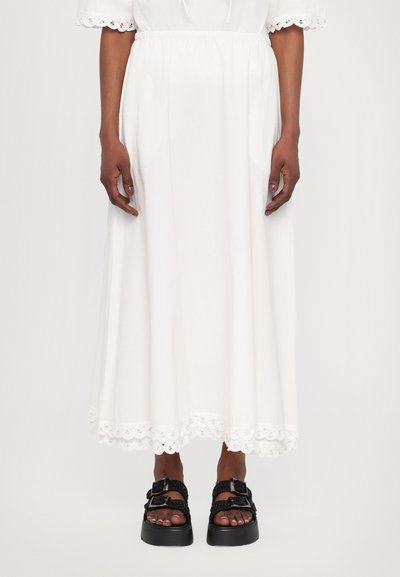 Jupe midi blanche au design fluide et à taille élastique. Dotée d'une finition en dentelle au bas. Associée à des sandales à plateforme noires.