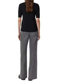 Zwart gebreid topje met korte mouwen, gecombineerd met hooggewaisted, losvallende grijze denim jeans. De outfit heeft een schone, minimalistische uitstraling.