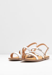 Witte leren sandalen met gevlochten bandjes, open teenontwerp, verstelbare enkelband en een tan lederen binnenzool. Vlakke zoolconstructie.