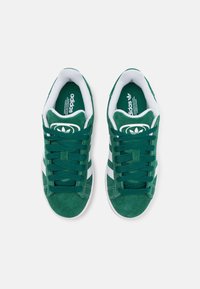 Baskets en daim vert avec accents blancs, présentant un design classique à lacets, une surface texturée et un logo imprimé sur la languette.