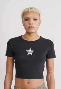 Svart kortärmad t-shirt i ribbad tyg med en vit stjärndesign och ordet "OBEY" i en cirkulär form i mitten.