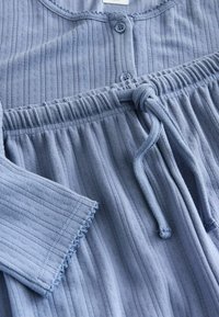 Pehme sinine soonikkoega vabaajariiete komplekt, mis sisaldab nööpidega avanevat pusa ja elastse vöökohaga pükse, millel on nööriga seotav pael ja sakilise servaga varrukad.