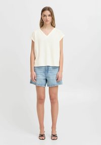 Krémový krátký rukávový top s V-výstřihem, spárovaný se světle modrými denimovými šortkami. Minimalistický design s volným střihem.