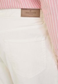 Pantalones de algodón blancos con una etiqueta de cuero de Hackett London. Presentan un bolsillo trasero único con costura curva y una textura suave.