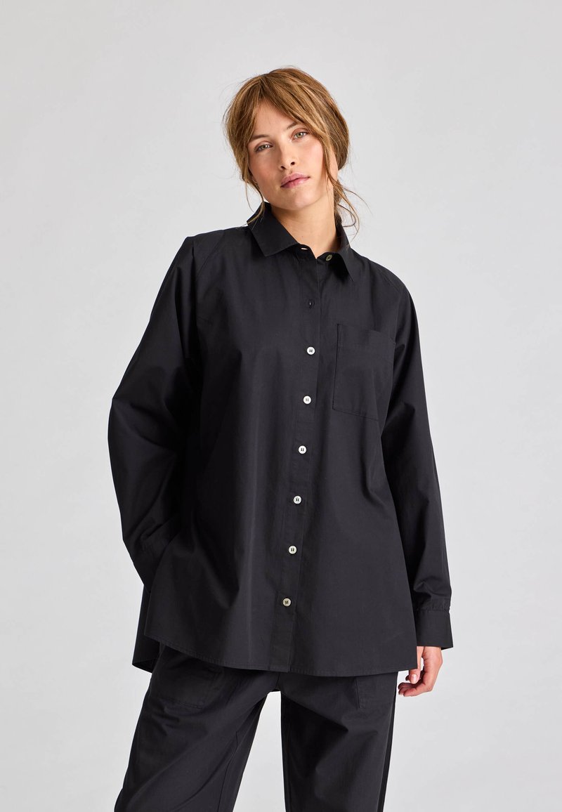 Sort skjorte med knapper lavet af bomuld, med krave, lange ærmer og en brystlomme. Har sølvknapper og en afslappet pasform.