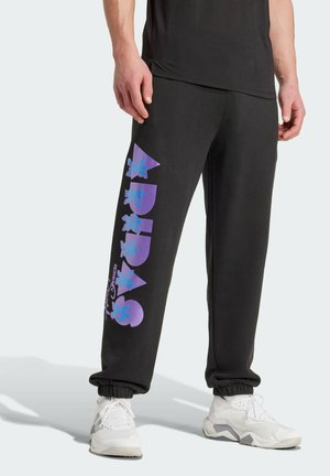 Pantalons de survêtement noirs avec des graphismes violets sur la jambe gauche ; poignets élastiques et coupe décontractée. Le tissu semble doux avec une texture lisse.