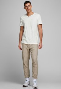 Lichtgekleurde crème, t-shirt met korte mouwen en een v-hals met twee knopen. Gecombineerd met lichtbeige, relaxed-fit broeken en witte sneakers.