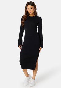 Abito midi a maglia nera a coste con maniche lunghe e spacchi laterali, dotato di collo a giro e silhouette aderente, abbinato a sneakers bianche.