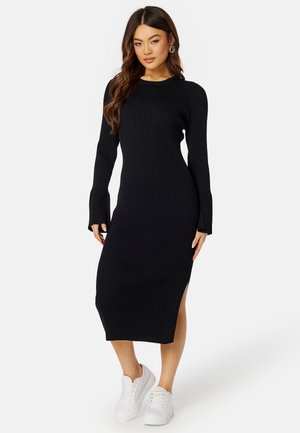 Abito midi a maglia nera a coste con maniche lunghe e spacchi laterali, dotato di collo a giro e silhouette aderente, abbinato a sneakers bianche.