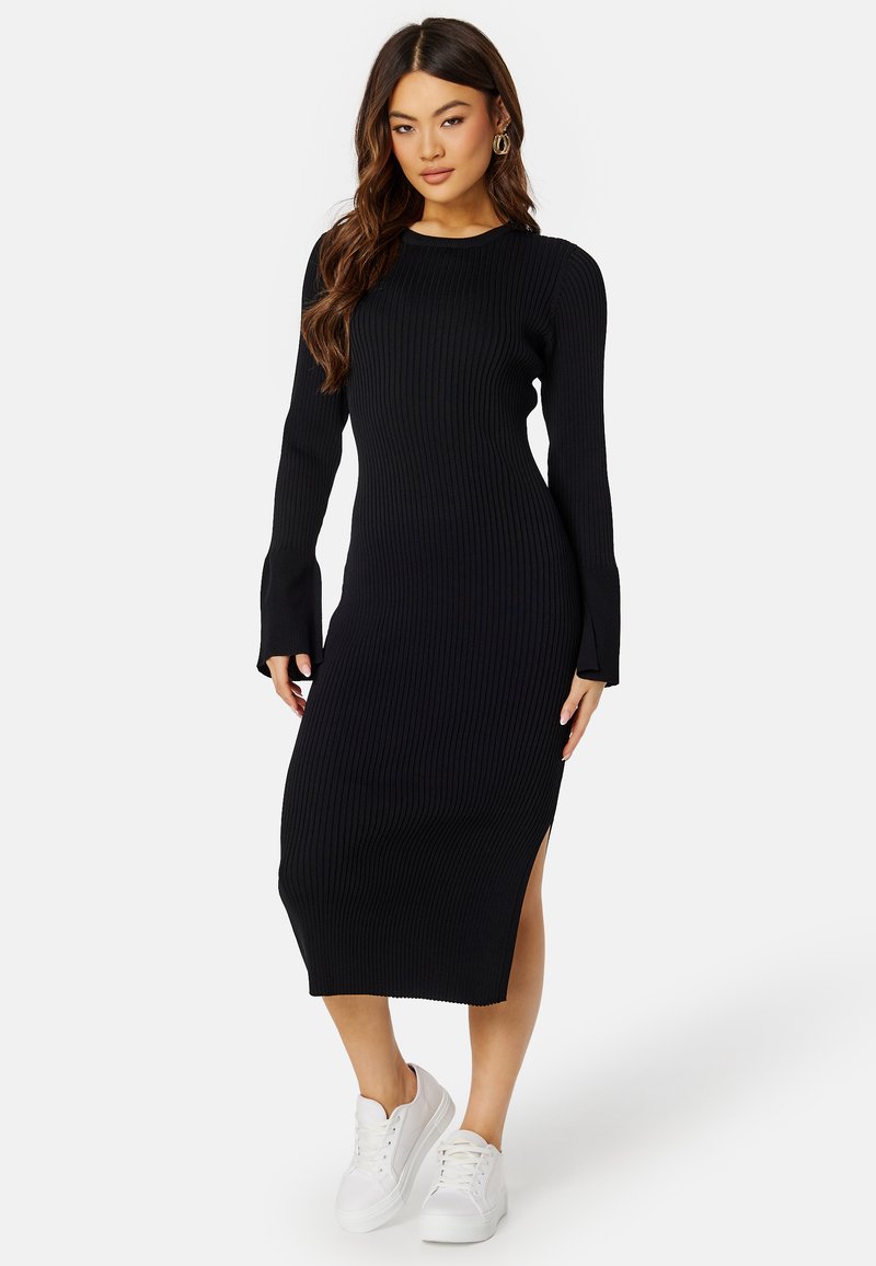 Abito midi a maglia nera a coste con maniche lunghe e spacchi laterali, dotato di collo a giro e silhouette aderente, abbinato a sneakers bianche.