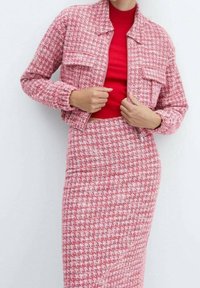 Veste en tweed rose au design court, avec deux poches avant et motif pied-de-poule texturé ; associée à une jupe crayon assortie. Haut rouge en dessous.