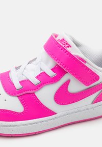 Nike tenisice s gornjim dijelom od bijele kože s jarkim ružičastim detaljima, čičak trakom i teksturiranom sivom potplatom.