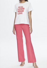 Camiseta blanca con texto rojo "SANAR APRENDER CRECER AMAR", combinada con pantalones de pierna ancha rosas. Tela suave y diseño simple.