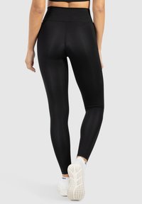 Zwarte high-waisted legging gemaakt van rekbaar materiaal, met een gladde textuur en een strakke pasvorm, gecombineerd met witte sportschoenen.