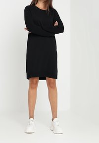 Svart stickad långärmad klänning med ribbad textur på ärmar och nederkant, tillsammans med vita stora sneakers.